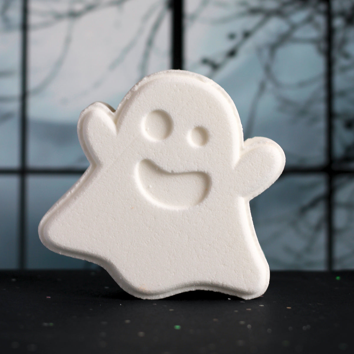 White ghost-shaped bath bomb on a dark surface with a blurred background