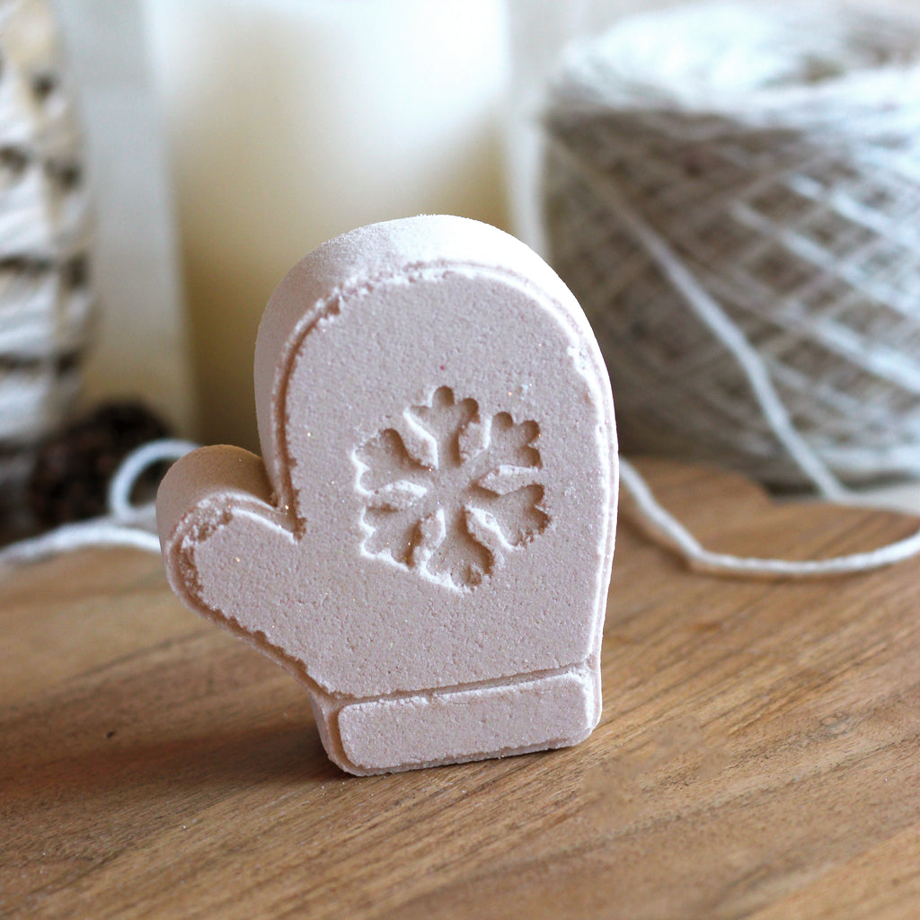 Tab mitten-shaped bath bomb with a snowflake design on a wooden surface.