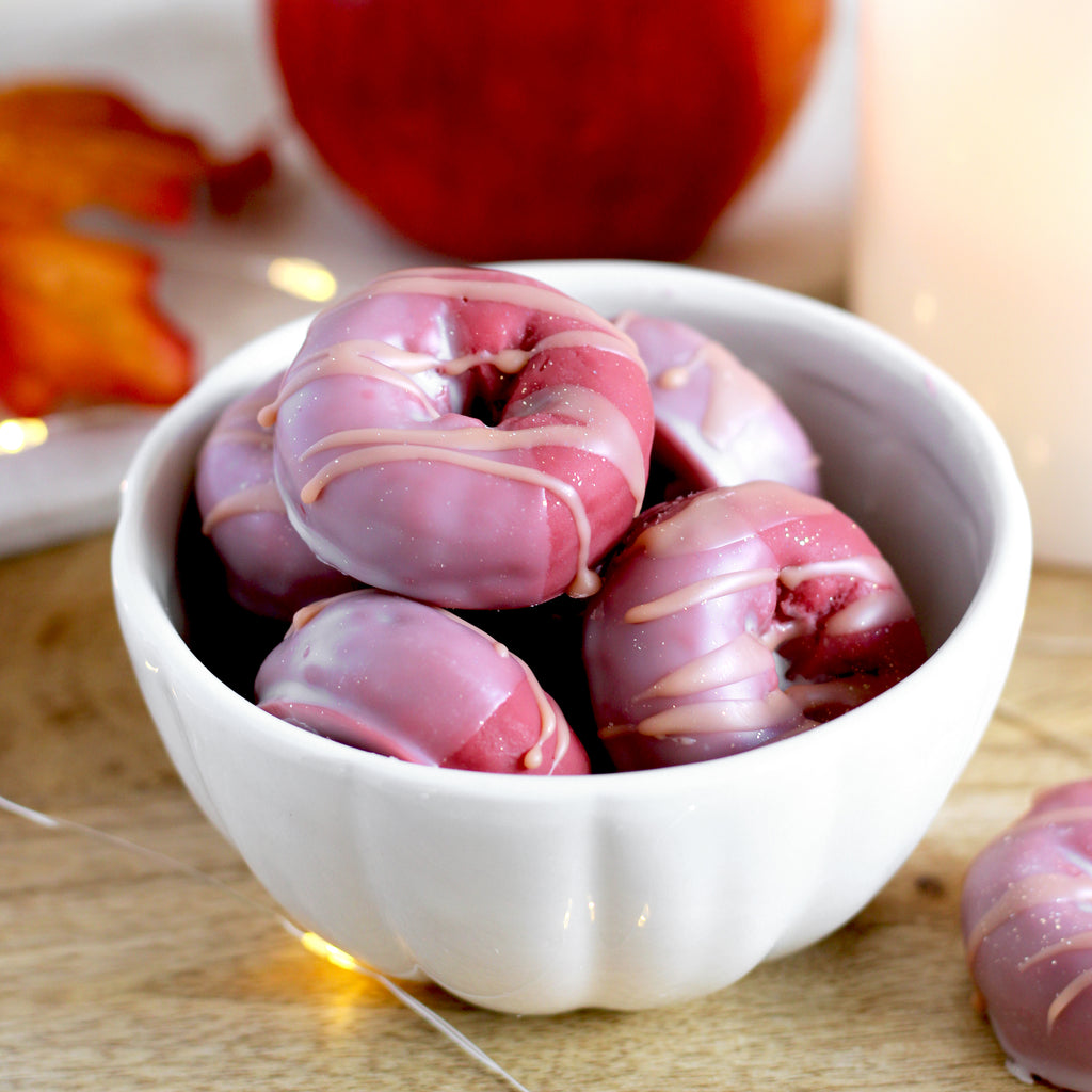 Pink donut-shaped wax melts in a white bowl on a wooden surface