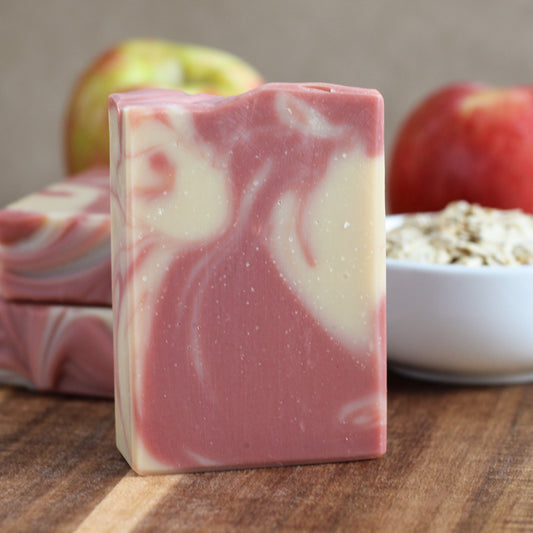 Apple & Oats handmade soap with soft red and creamy swirls, styled with red apples, oats, and warm autumn accents