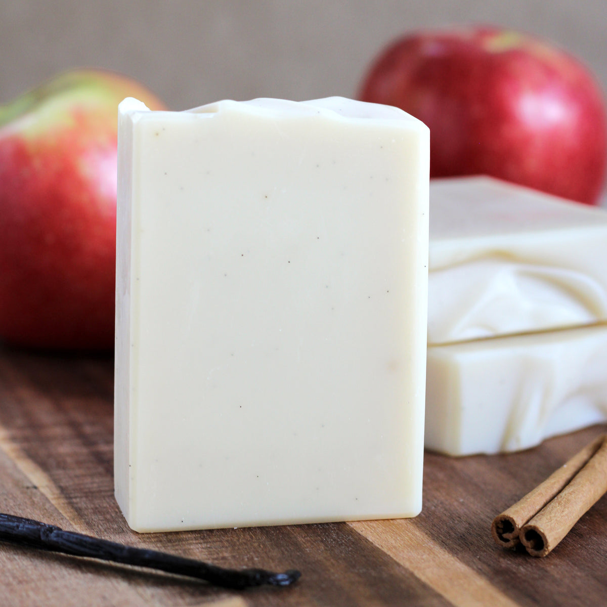 Apple Spice handmade soap with creamy swirls and vanilla bean specks, styled with red apples, cinnamon sticks, and vanilla beans.