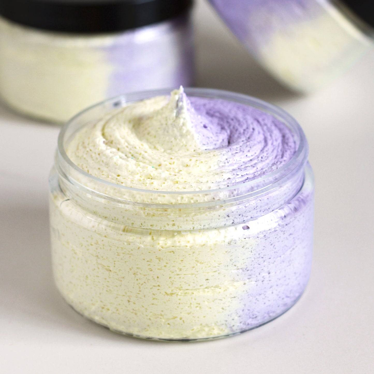 Missouri River Soap Berry Lemonade Whipped Soap Sugar Scrub in a 4 oz clear jar with one half yellow scrub and one purple scrub