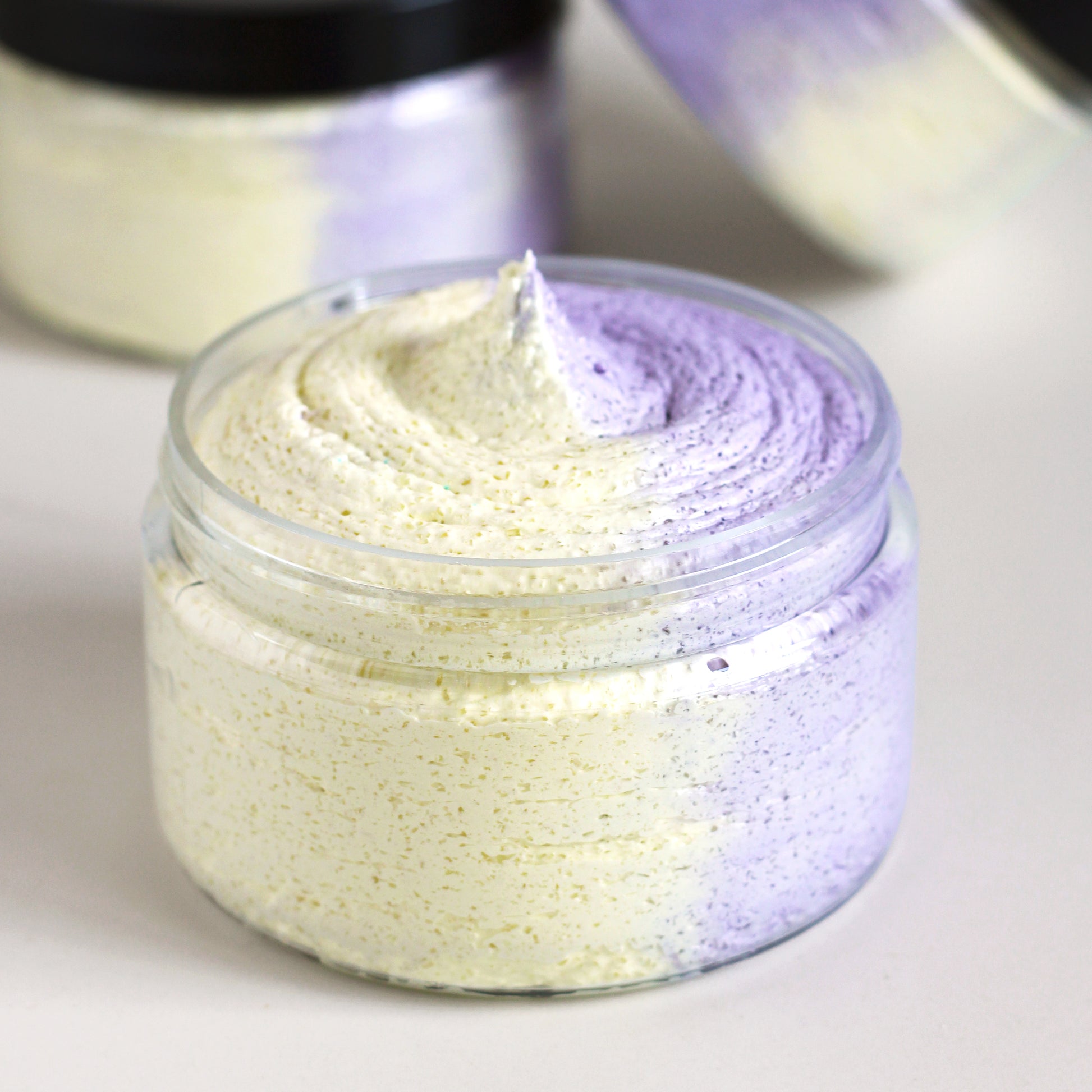 Missouri River Soap Berry Lemonade Whipped Soap Sugar Scrub in a 4 oz clear jar with one half yellow scrub and one purple scrub