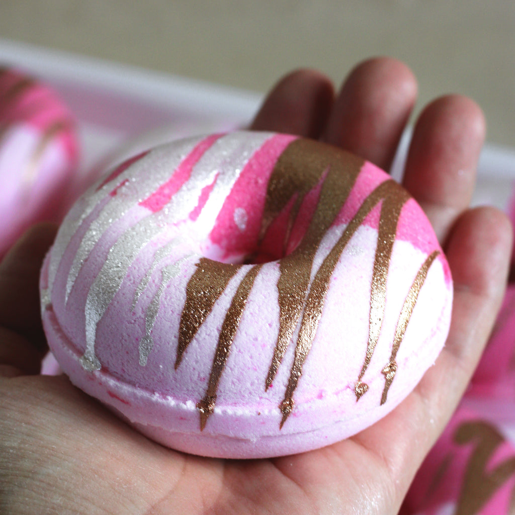Pink donut-shaped bath bombs with copper and white drizzle held in hand
