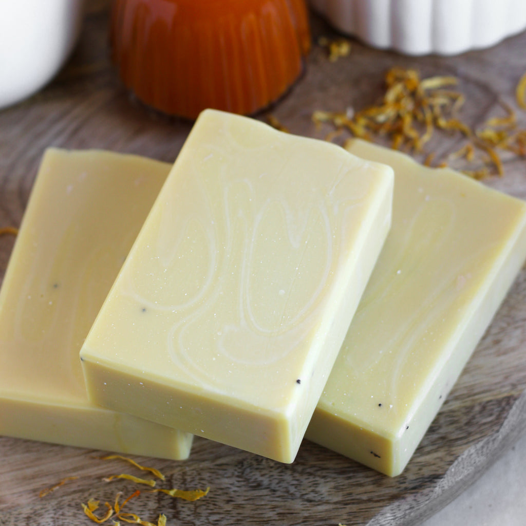 Three bars of yellow soap on a wooden surface with dried calendula.