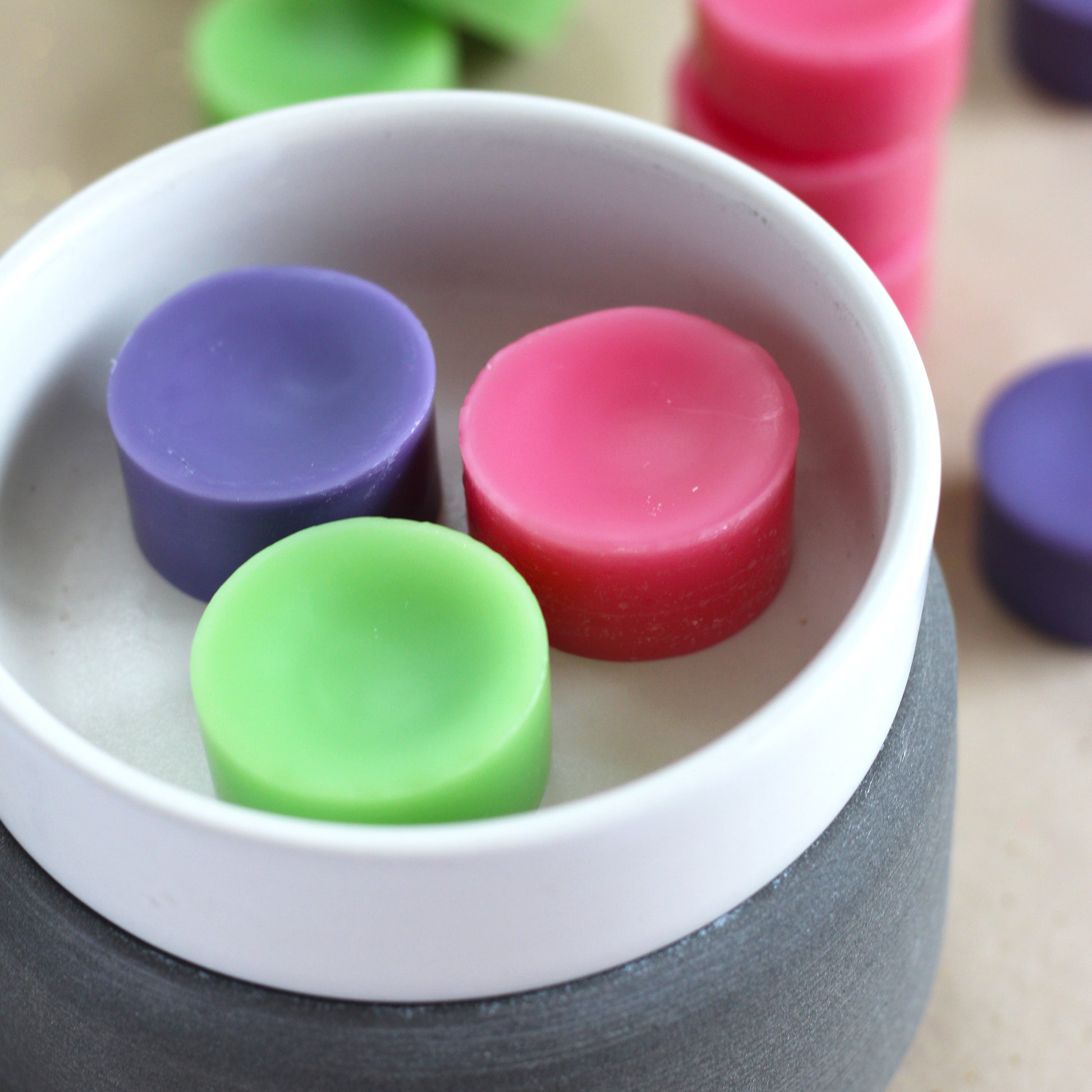 Green, pink, and purple disk-shaped wax melts in a bowl