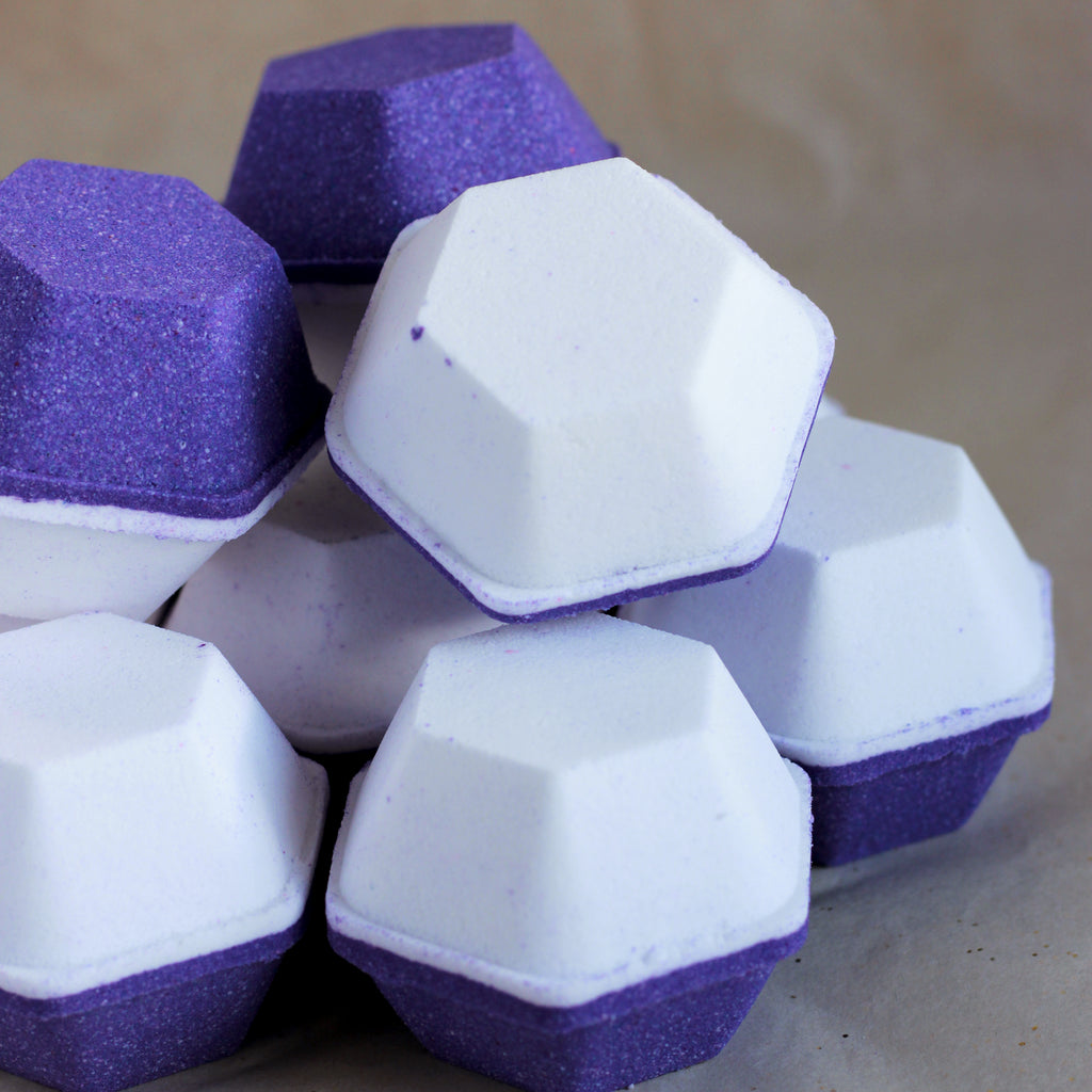 Purple and white bath bombs stacked on a neutral background