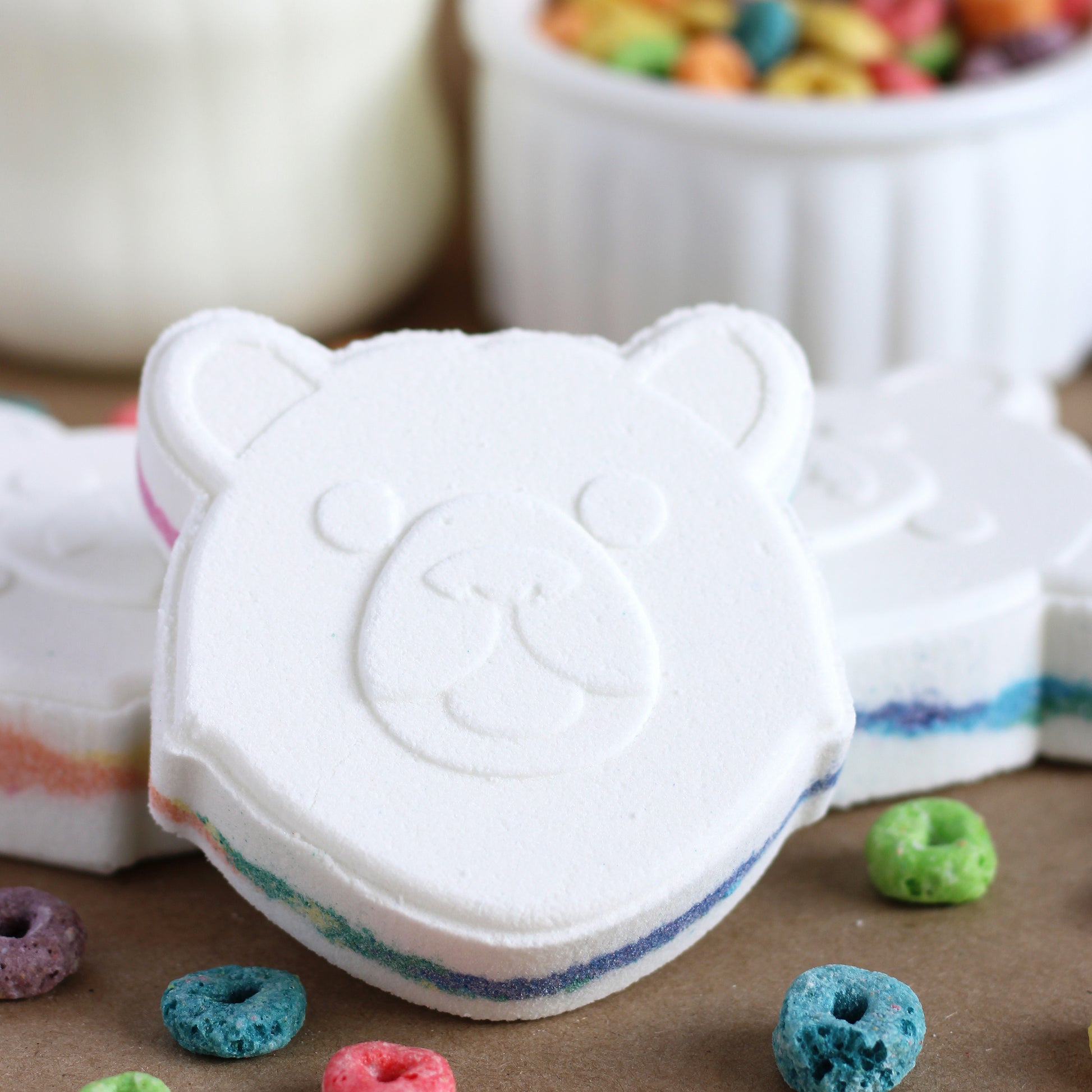 White bear-shaped bath bomb with rainbow center with colorful cereal pieces on a brown surface