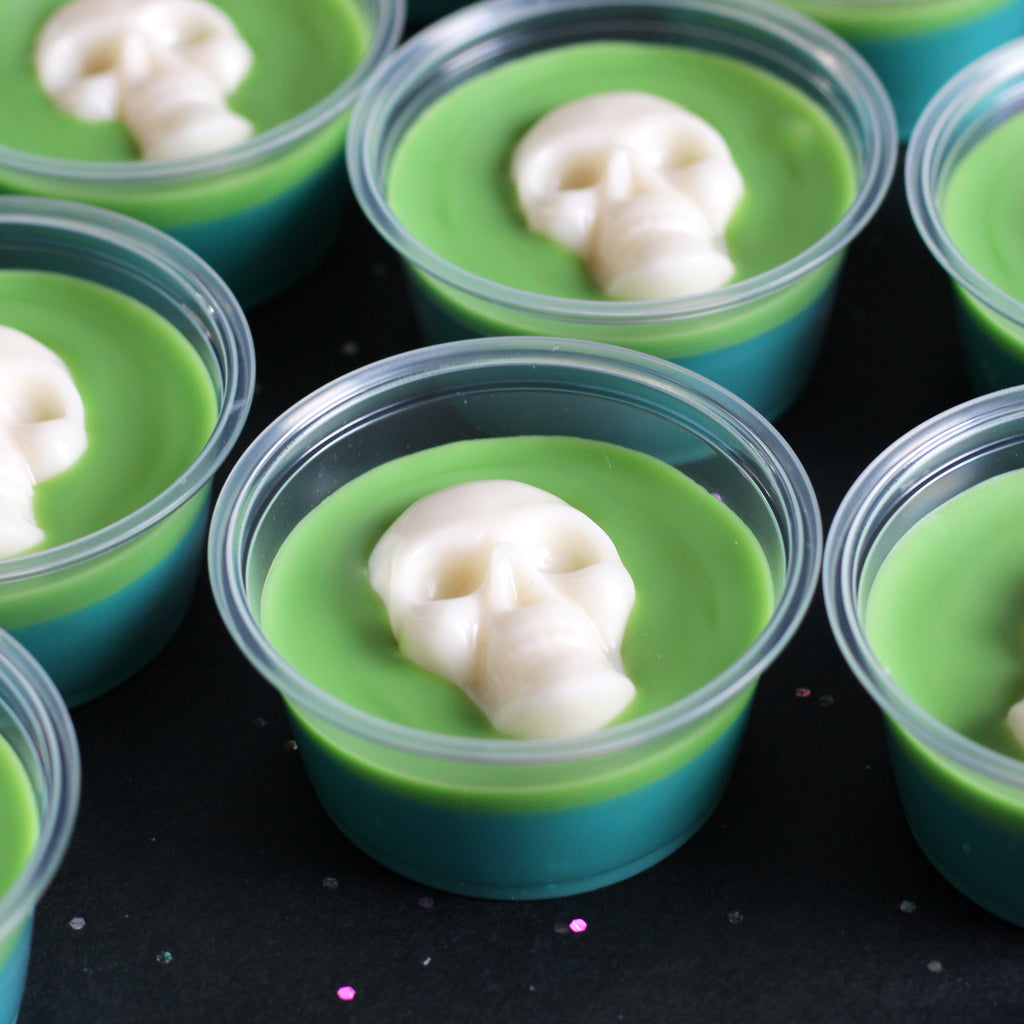 Green and blue wax melt cups with a white skull decorating the top