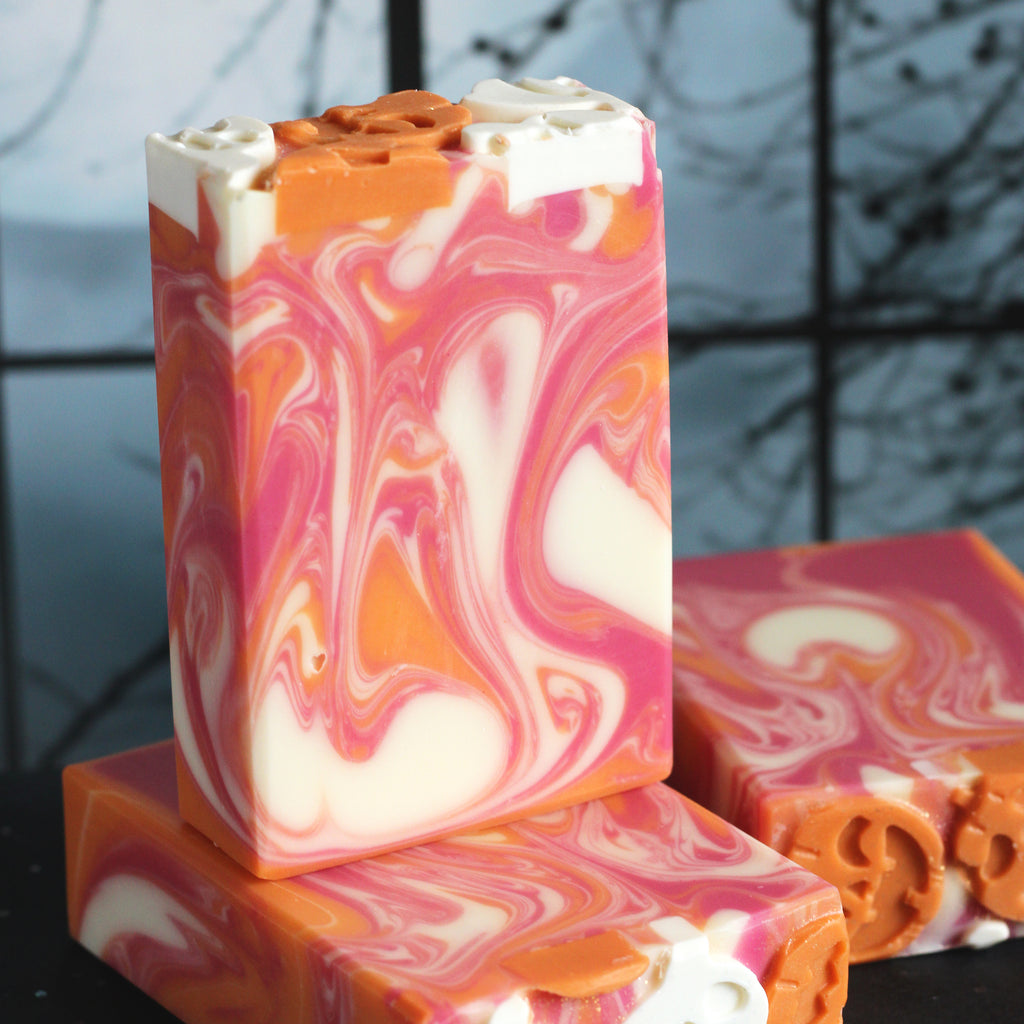 Soap bars in pink, orange, and white on a dark surface with a blurred background.