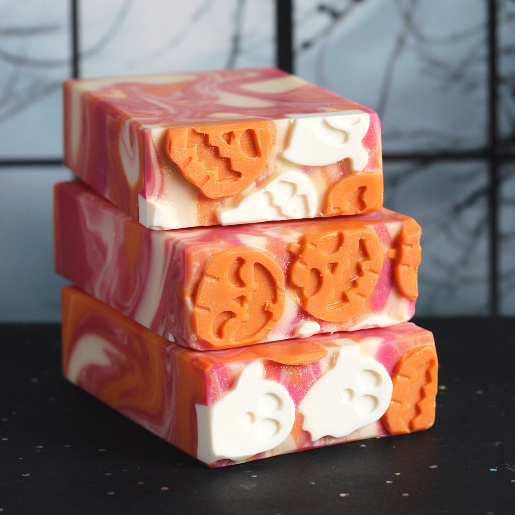 Stack of Halloween-themed soap bars with orange and white designs on a black surface.