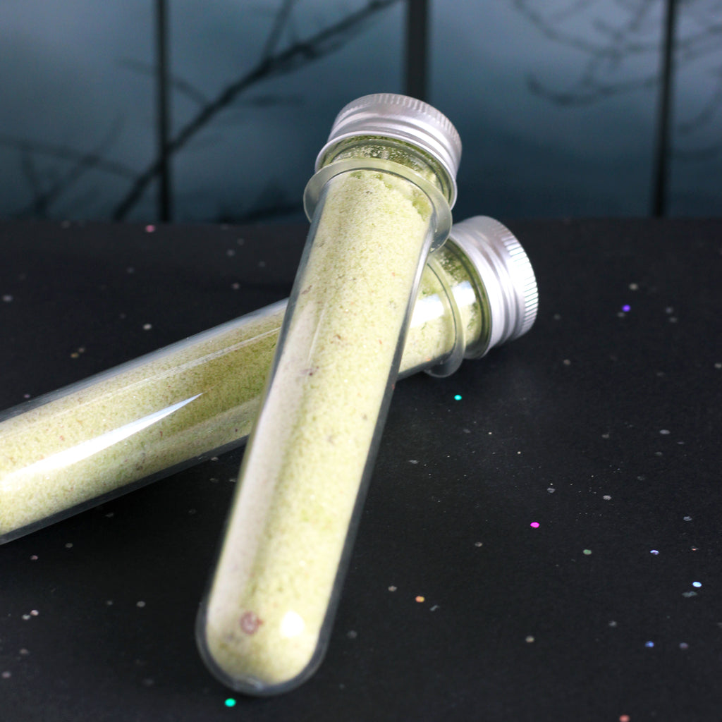 Two test tubes filled with yellowish-green bubbling bath salts on a dark surface.