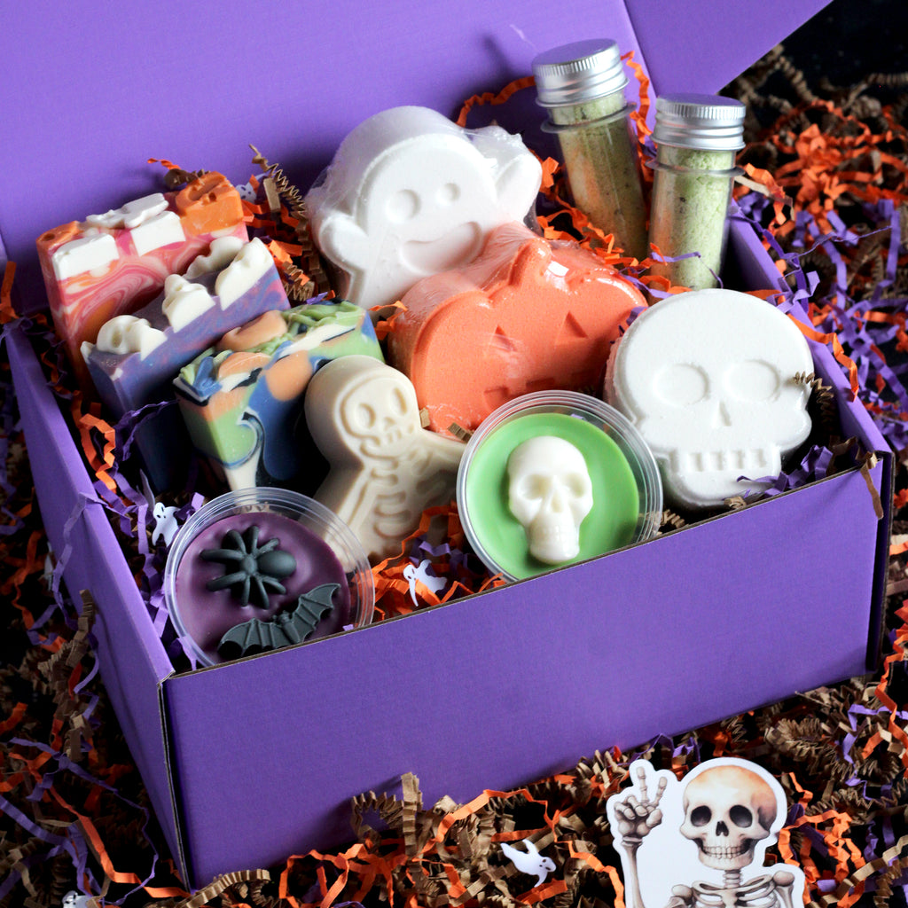 Assorted Halloween-themed soaps, bath bombs, bath salts, and wax melts in a purple box with decorative elements.