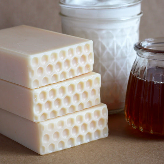 Three bars of honeycomb-patterned soap stacked with a jar of honey and yogurt in the background.