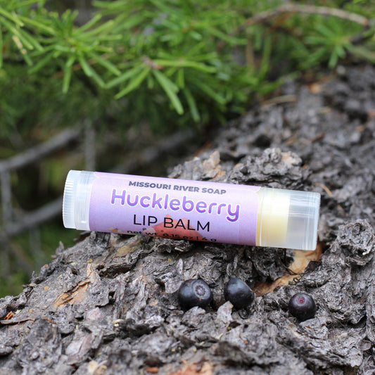 Huckleberry Lip Balm by Missouri River Soap photographed outdoors with huckleberries and evergreen branches