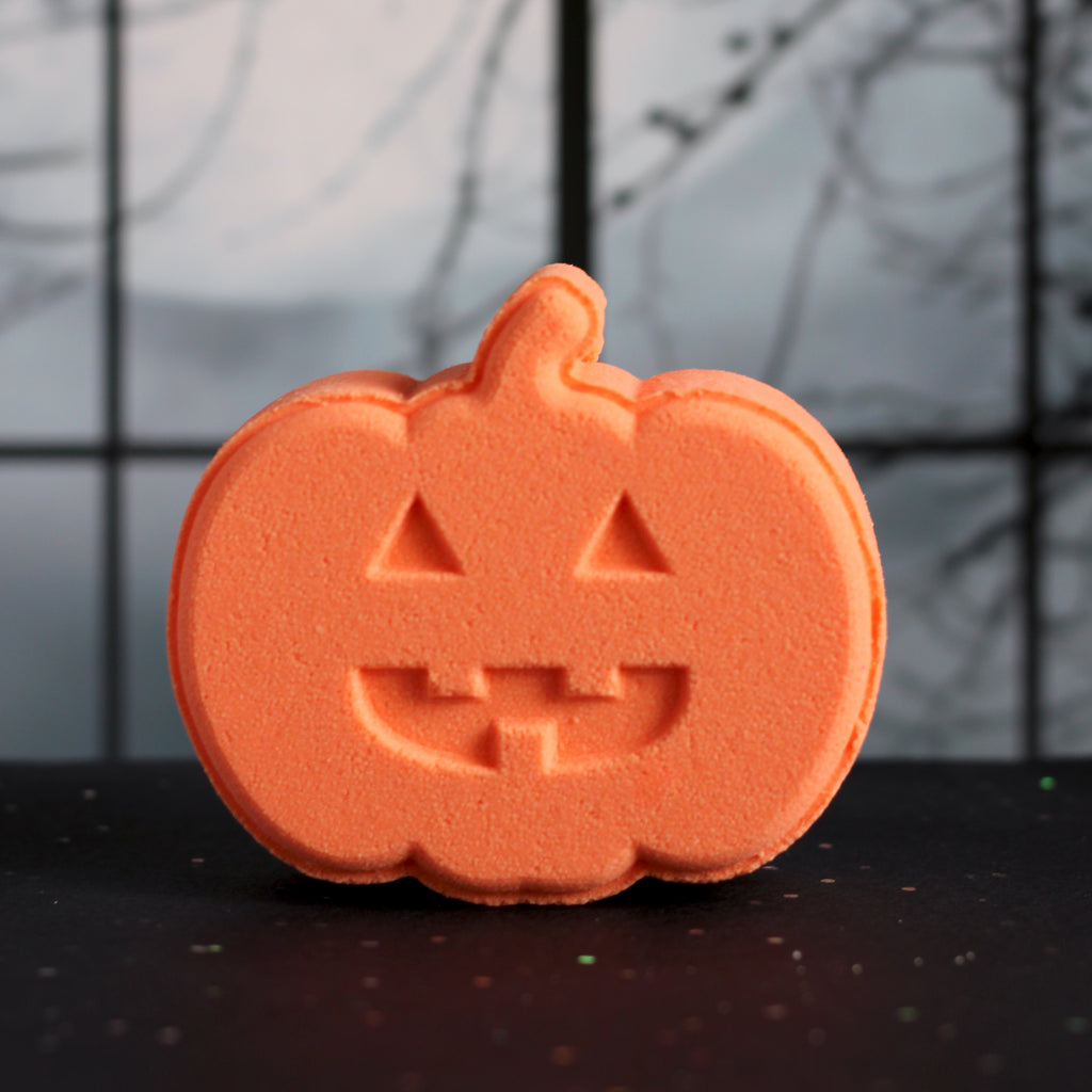 Orange jack o lantern shaped bath bomb on a black surface and spooky grey background