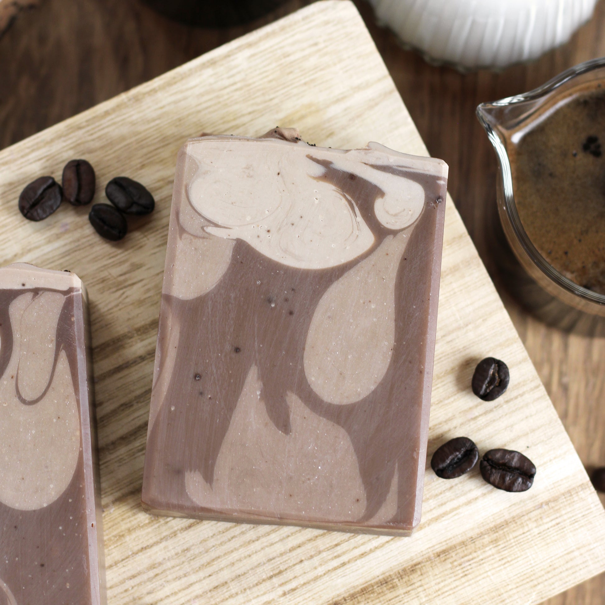 Coffee-themed soap bars on a wooden surface with coffee beans and a cup of coffee in the background.