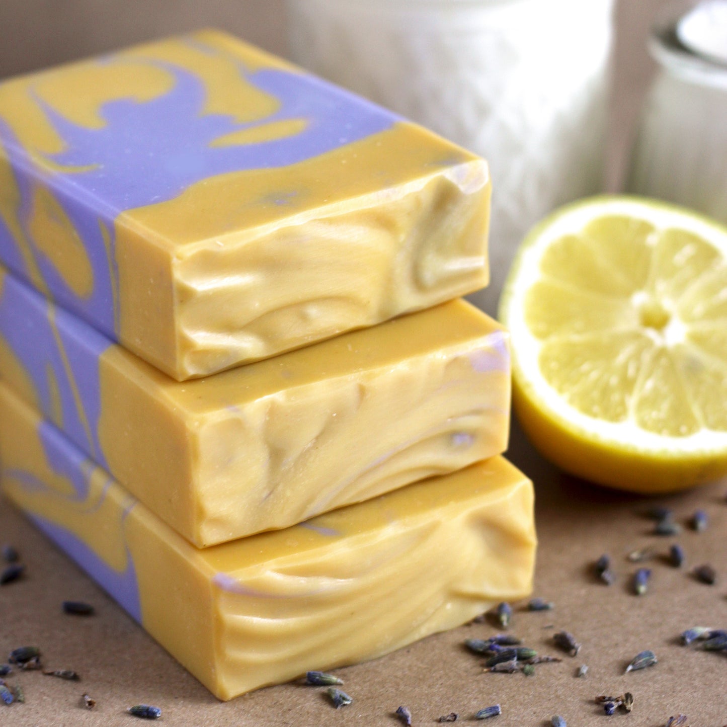 Three bars of yellow and purple swirled soap next to a lemon and lavender flowers on a brown surface.