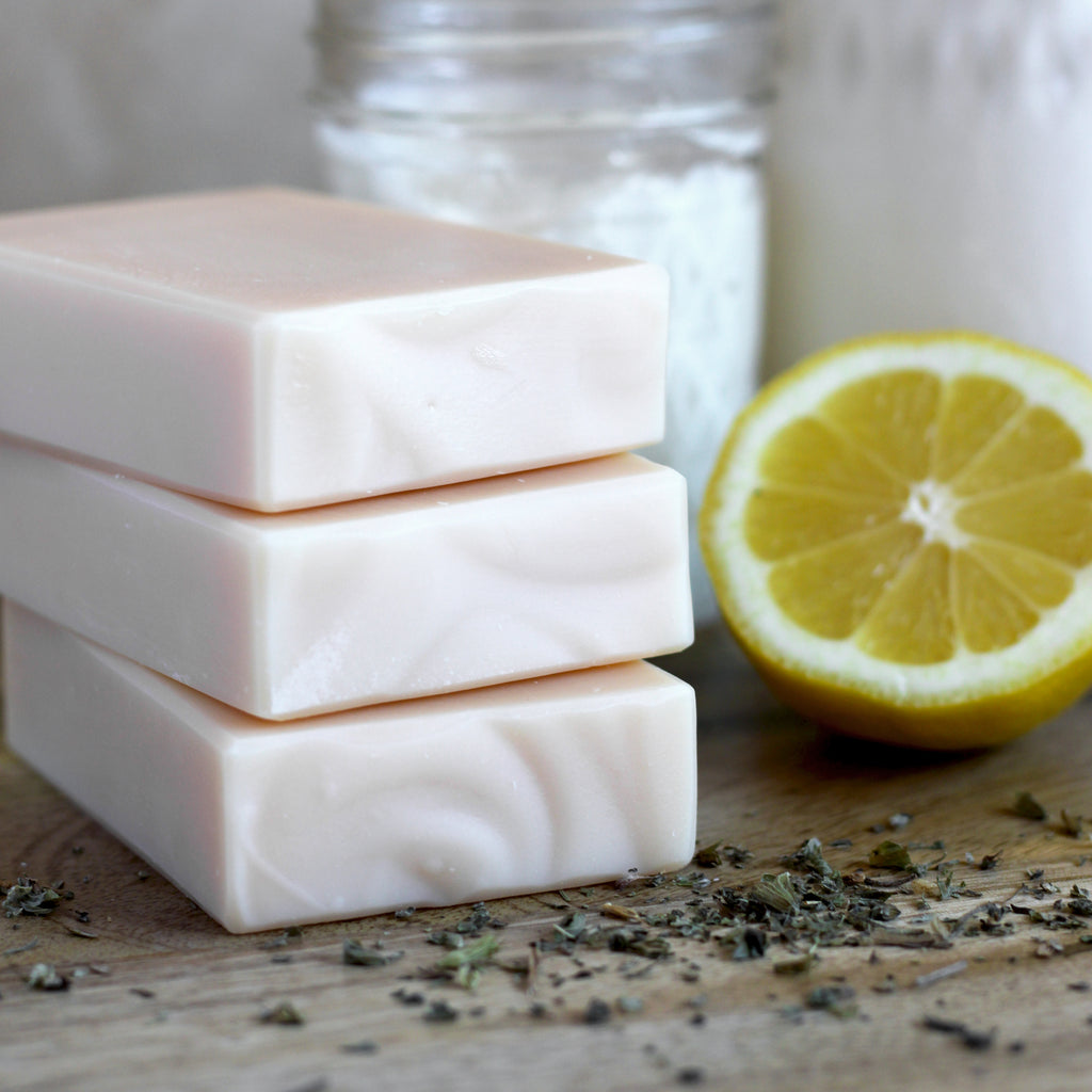 Three bars of soap stacked with a lemon and herbs on a wooden surface