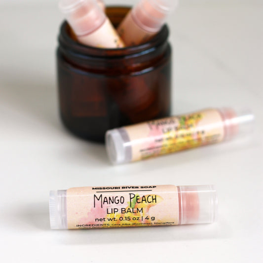 Mango Peach Lip Balm in a clear tube with a light peachy balm, handcrafted with mango butter, beeswax, and botanical oils. Features a bright mango peach fragrance with a subtle shimmer.