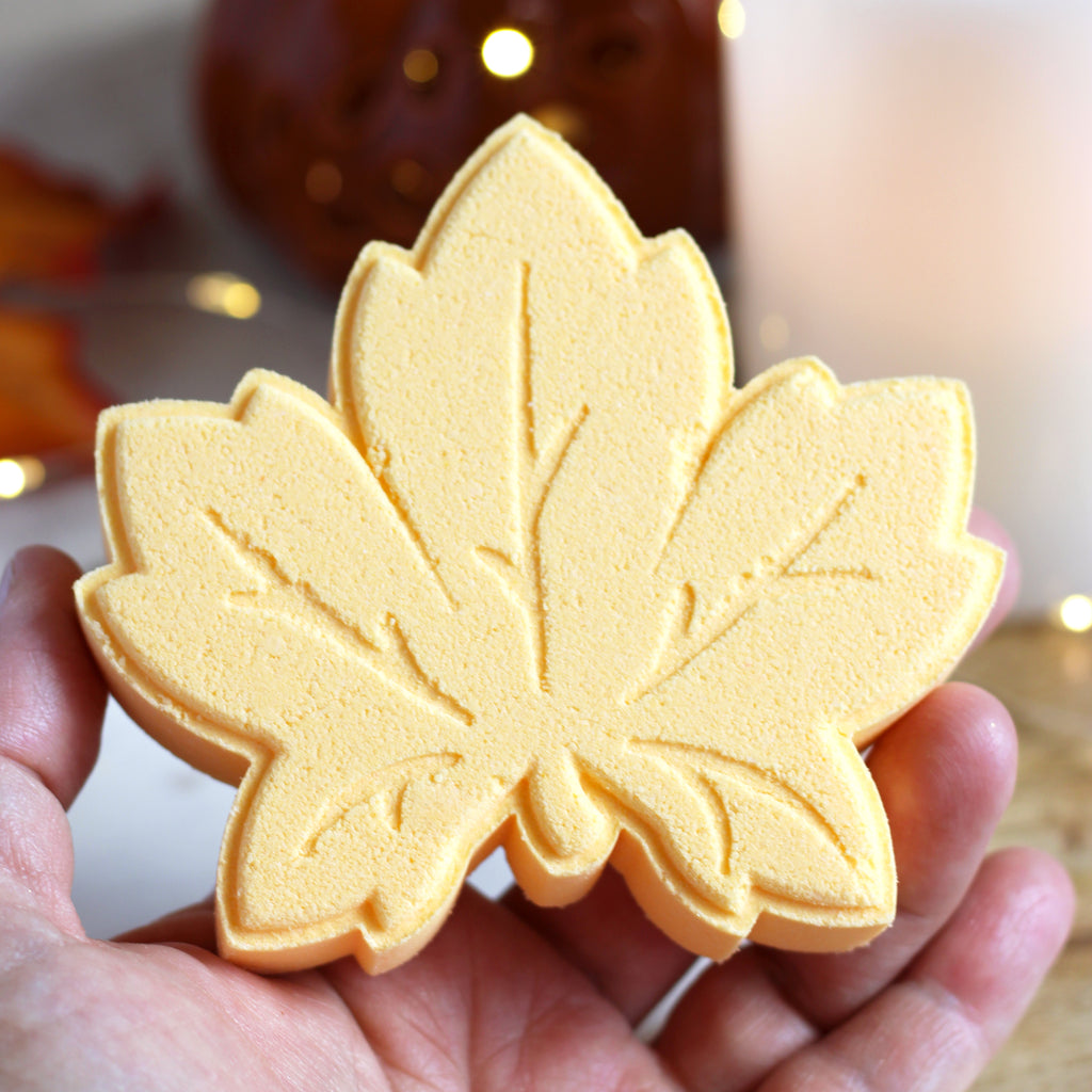 Yellow leaf-shaped bath bomb held in a hand with a blurred background