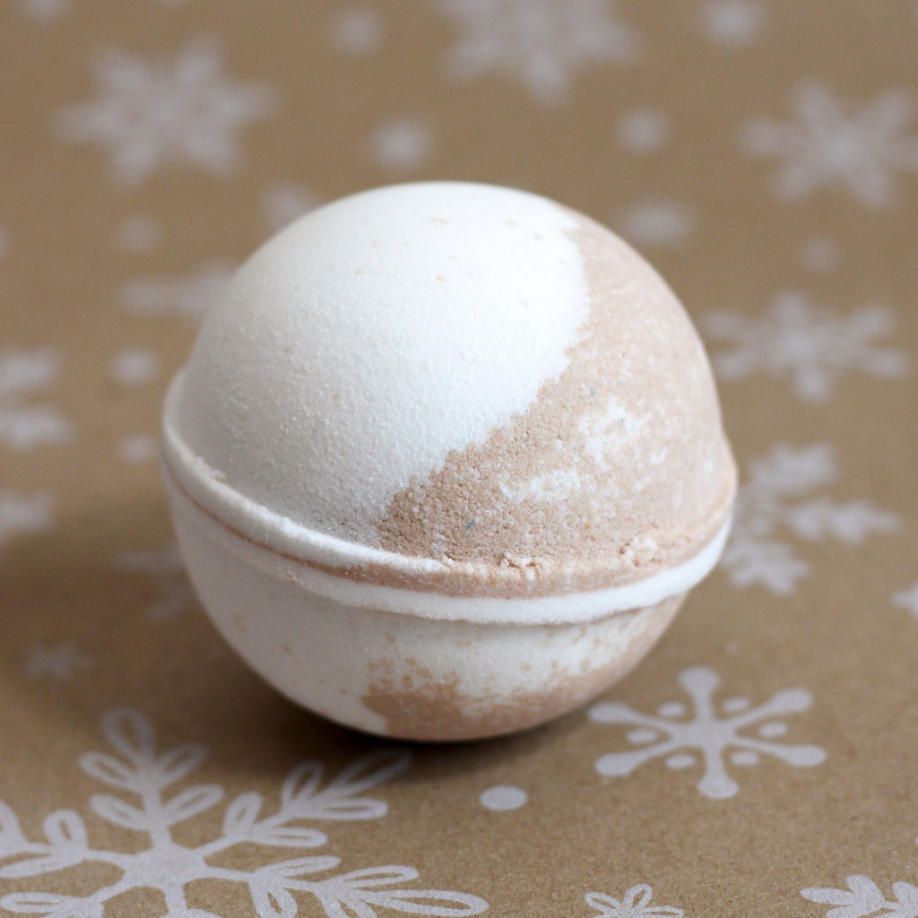 Milk & Honey bath bomb in white and honey-brown swirls, on a snowflake-printed kraft background