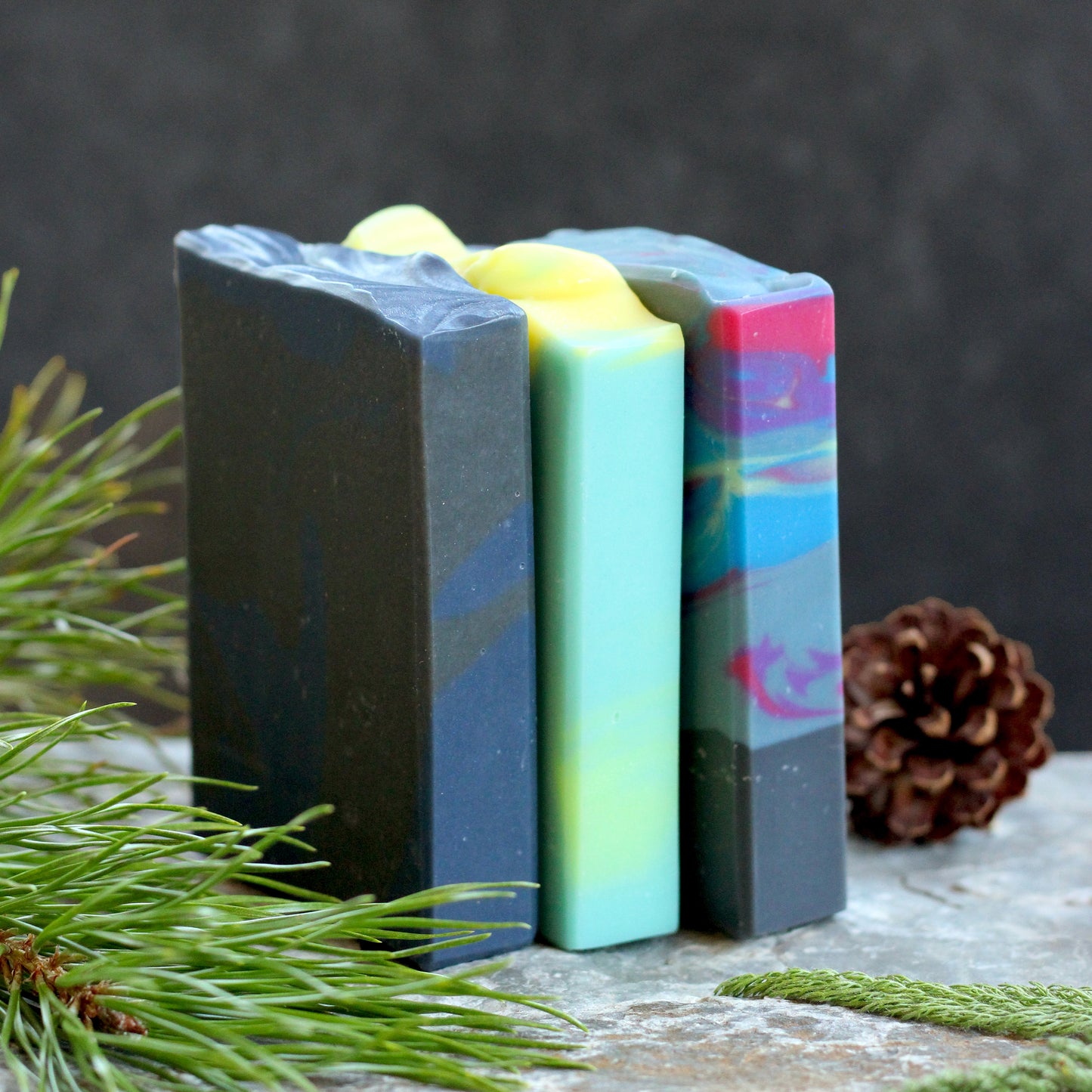 Missouri River Soap Night Sky Soap Sampler featuring three handcrafted artisan soaps inspired by summer nights, photographed with evergreen sprigs and pinecones on a rustic stone surface