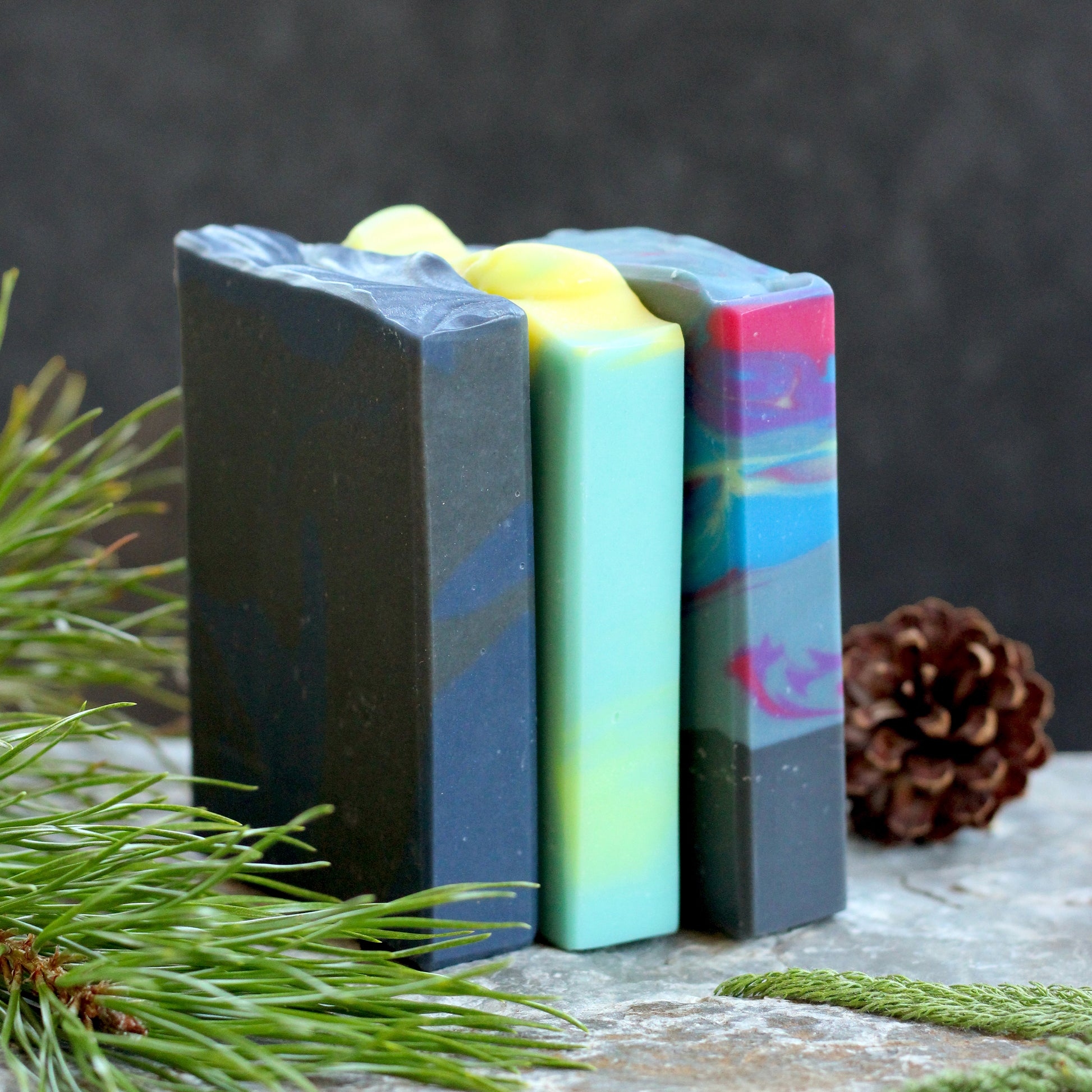 Missouri River Soap Night Sky Soap Sampler featuring three handcrafted artisan soaps inspired by summer nights, photographed with evergreen sprigs and pinecones on a rustic stone surface