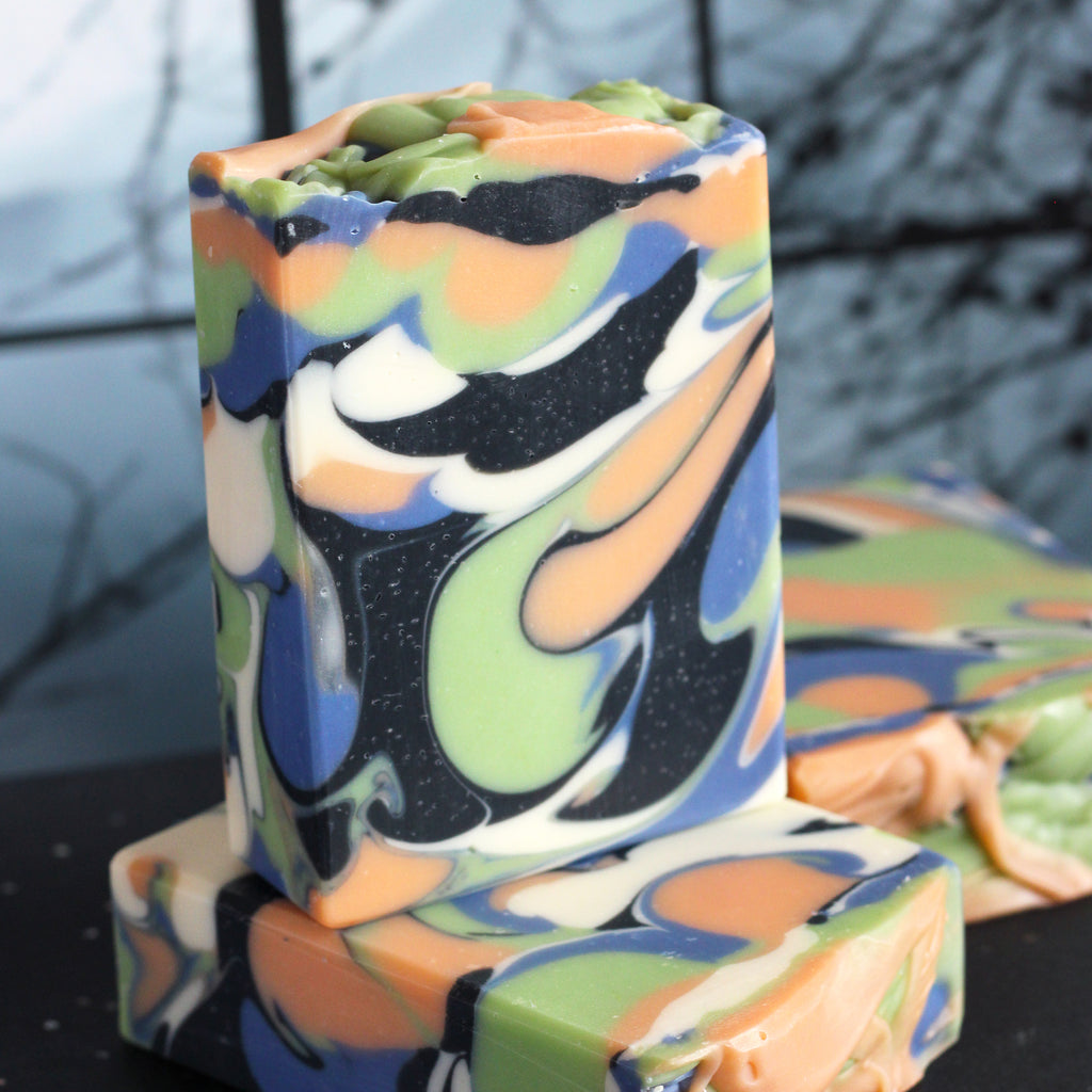 White, orange, green, blue, and black swirled soap on a dark surface with a blurry background.
