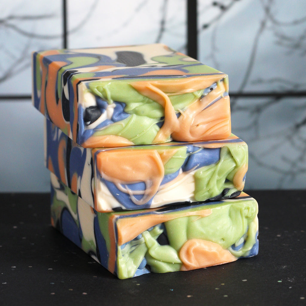 White, orange, green, blue, and black swirled soap on a dark surface with a blurry background.
