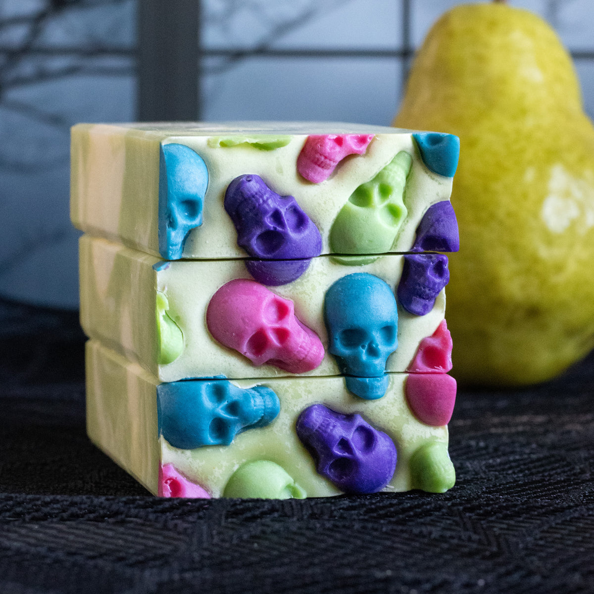Pearanormal pear-scented handmade soap with colorful skull embeds stacked beside a fresh pear