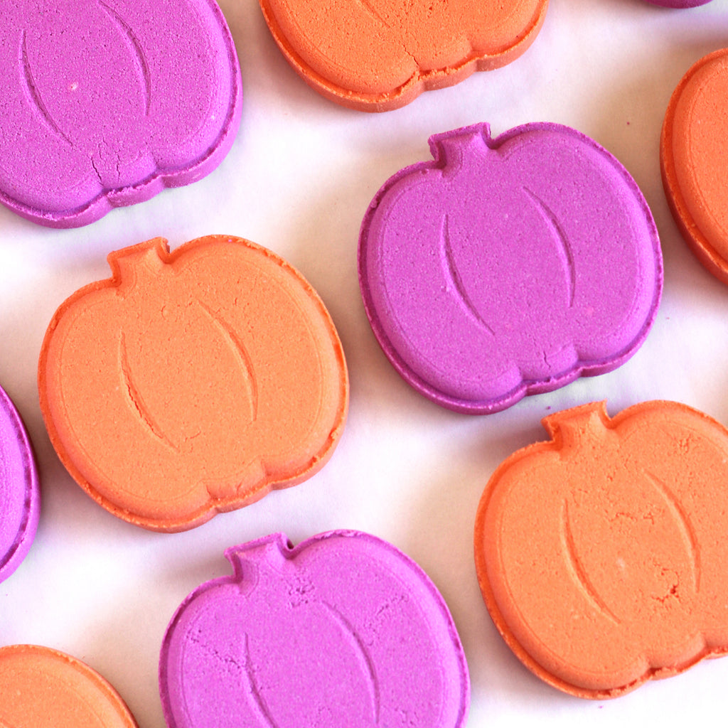 Pink and orange flat pumpkin-shaped bath bombs on a white background