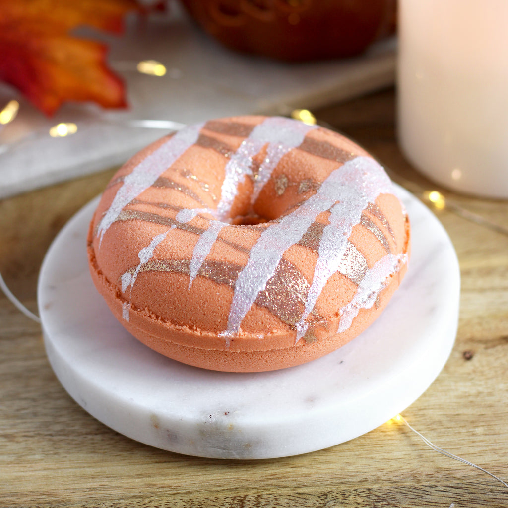Pumpkin donut-shaped bath bomb with white glaze on a marble coaster with a blurred background