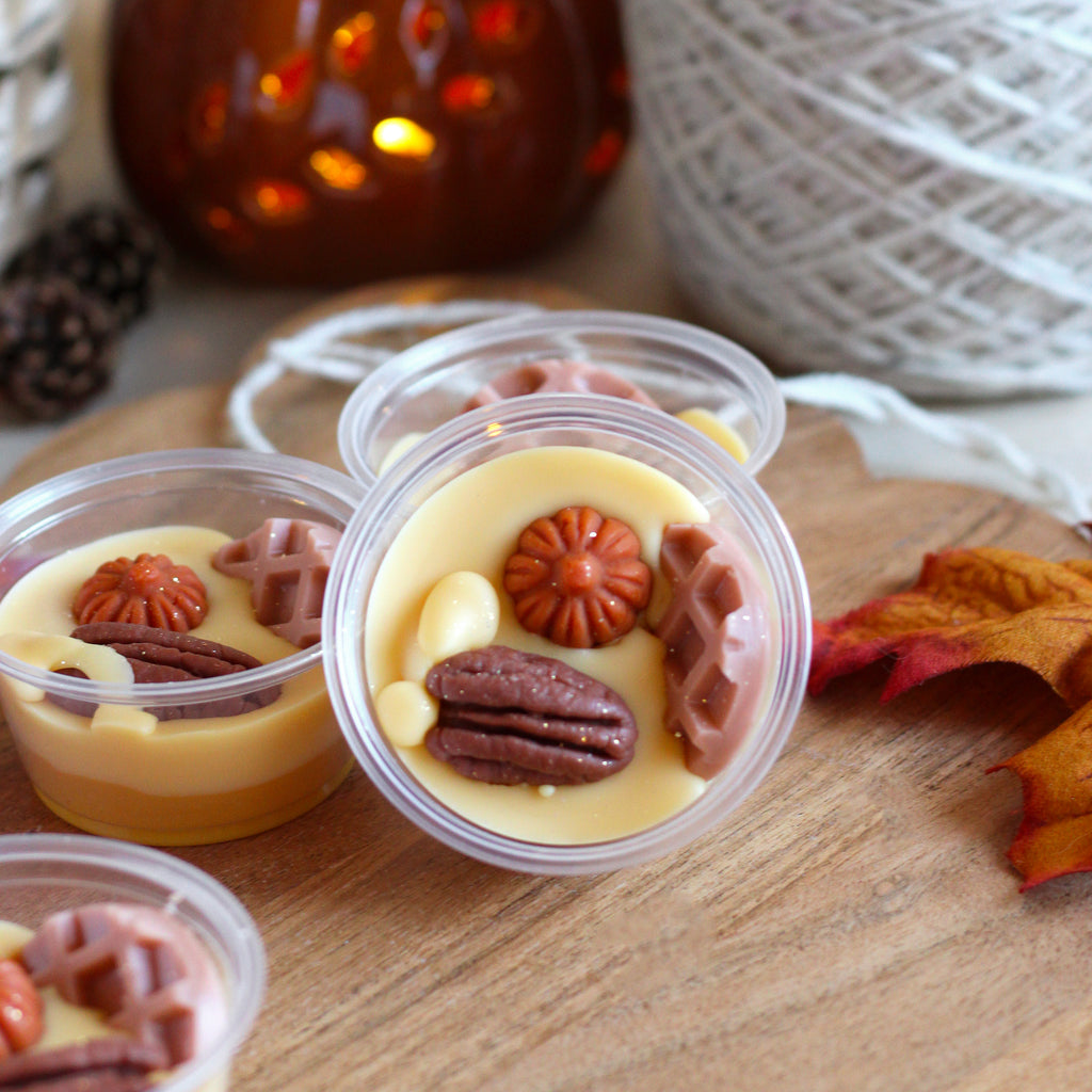 Small plastic cup with a creamy yellow wax and pumpkin, pecan, and waffle shapes on a wooden surface.