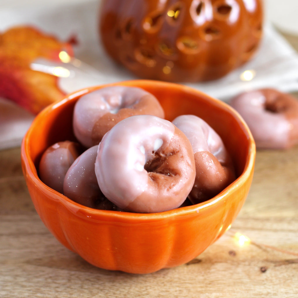 Pumpkin-shaped bowl filled with small donut-like wax melts on a wooden surface.