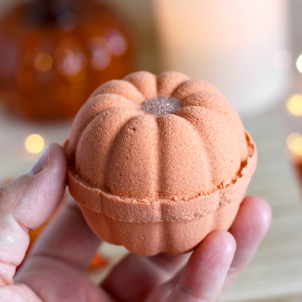Pumpkin-shaped bath bomb held in a hand with blurred pumpkins and lights in the background