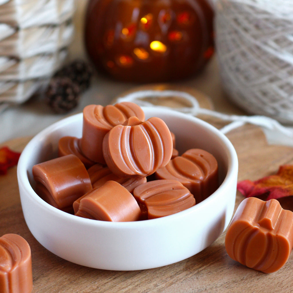 Small pumpkin shaped wax melts in a bowl on a wooden surface