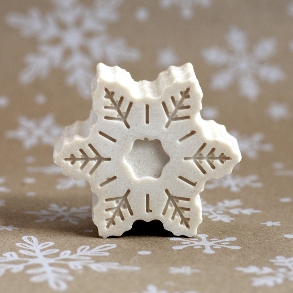 Sad Snowflake Sea Salt Soap bar with a tan snowflake design, on a snowflake-printed kraft background