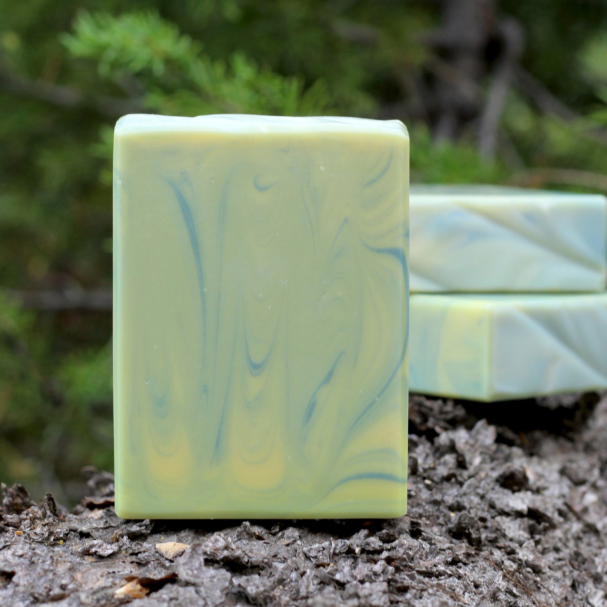 Missouri River Soap Sierra Sounds artisan soap with yellow, soft sage green and blue marbling, photographed outdoors on textured tree bark with a forest backdrop