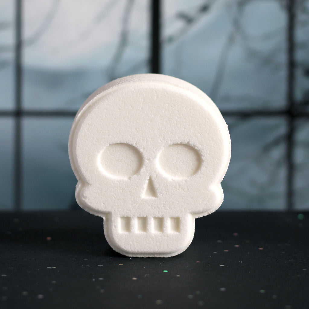 White skull-shaped bath bomb on a dark surface with a blurred background