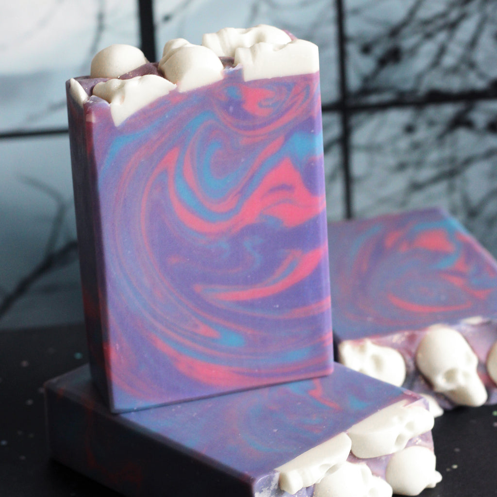 Swirled purple, blue and pink soap bar with white skull embeds on a dark background