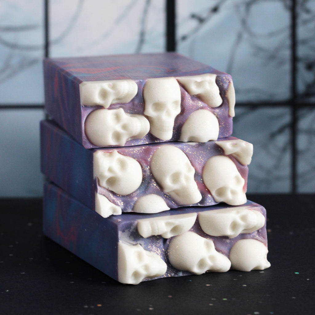 Three bars of soap with skull designs stacked on a dark surface with a blurred background.