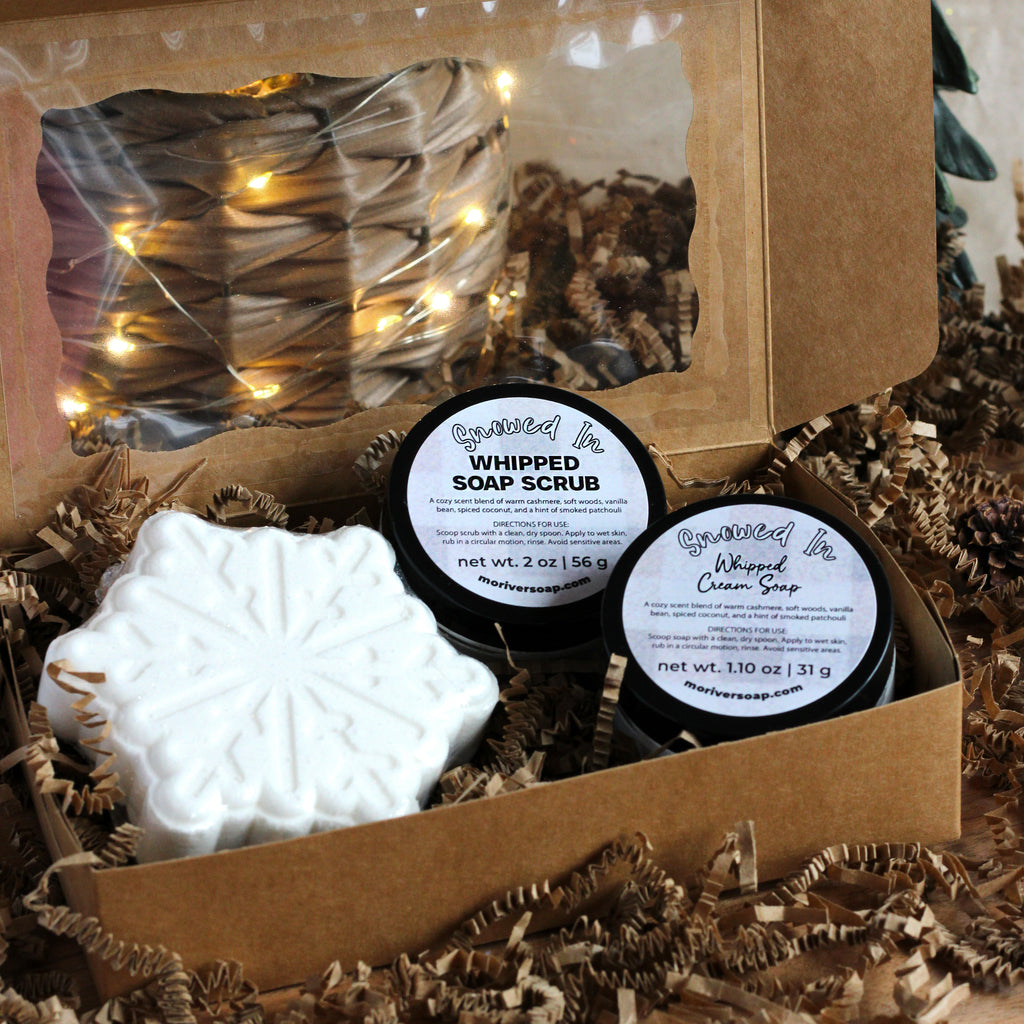 Three Snowed In products in a box with string lights in the background.