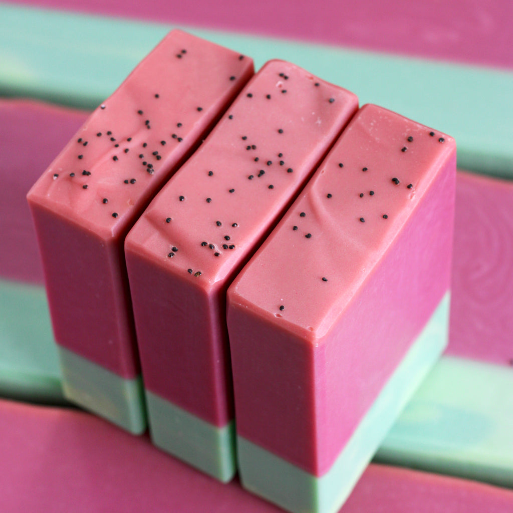 Three pink soap bars with black specks on a colorful background