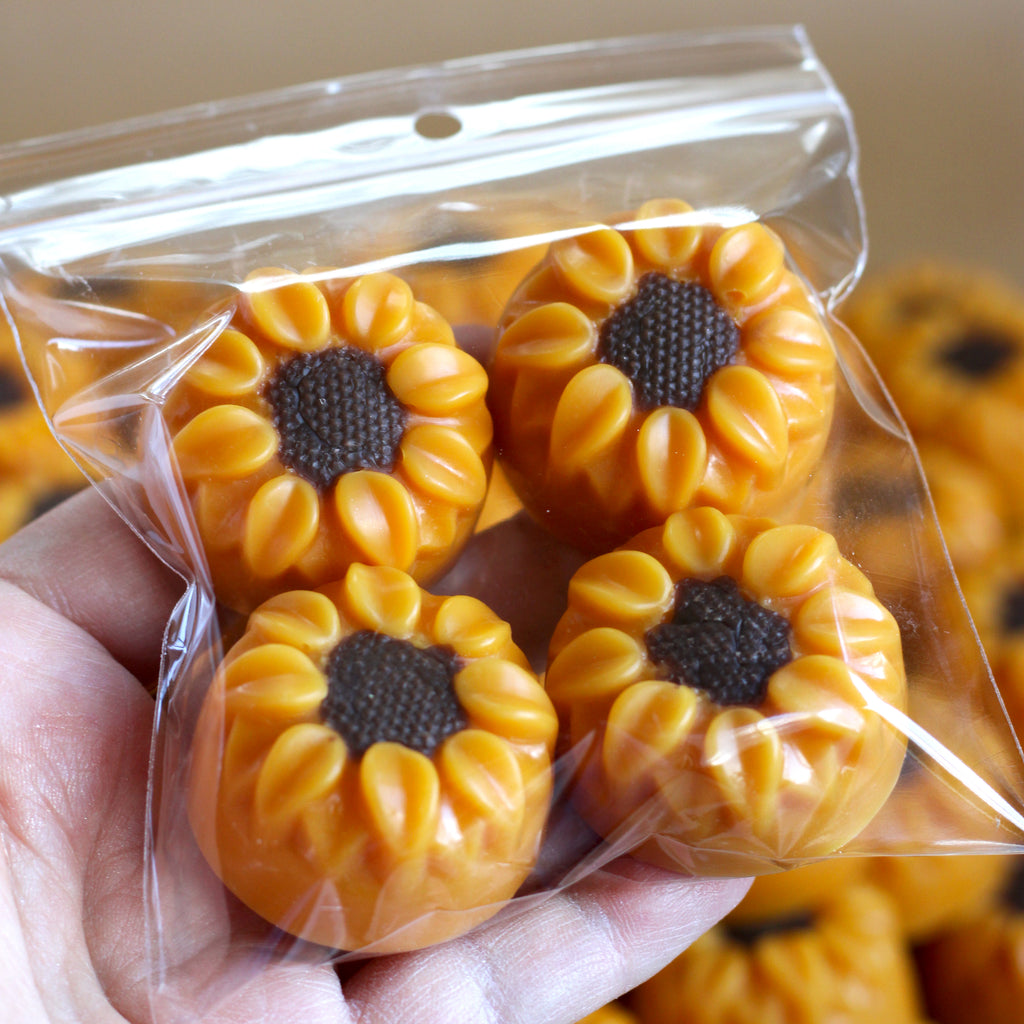 Sunflower-shaped wax melts in a clear plastic bag held by a hand.