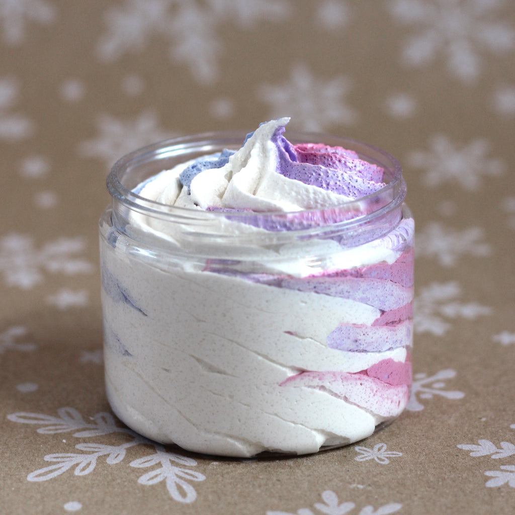 Wild Berry Blizzard whipped soap sugar scrub in a clear jar with white, pink, purple, and blue swirls on a kraft snowflake background