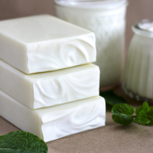 Stack of pale green soap bars with mint leaves on a neutral background