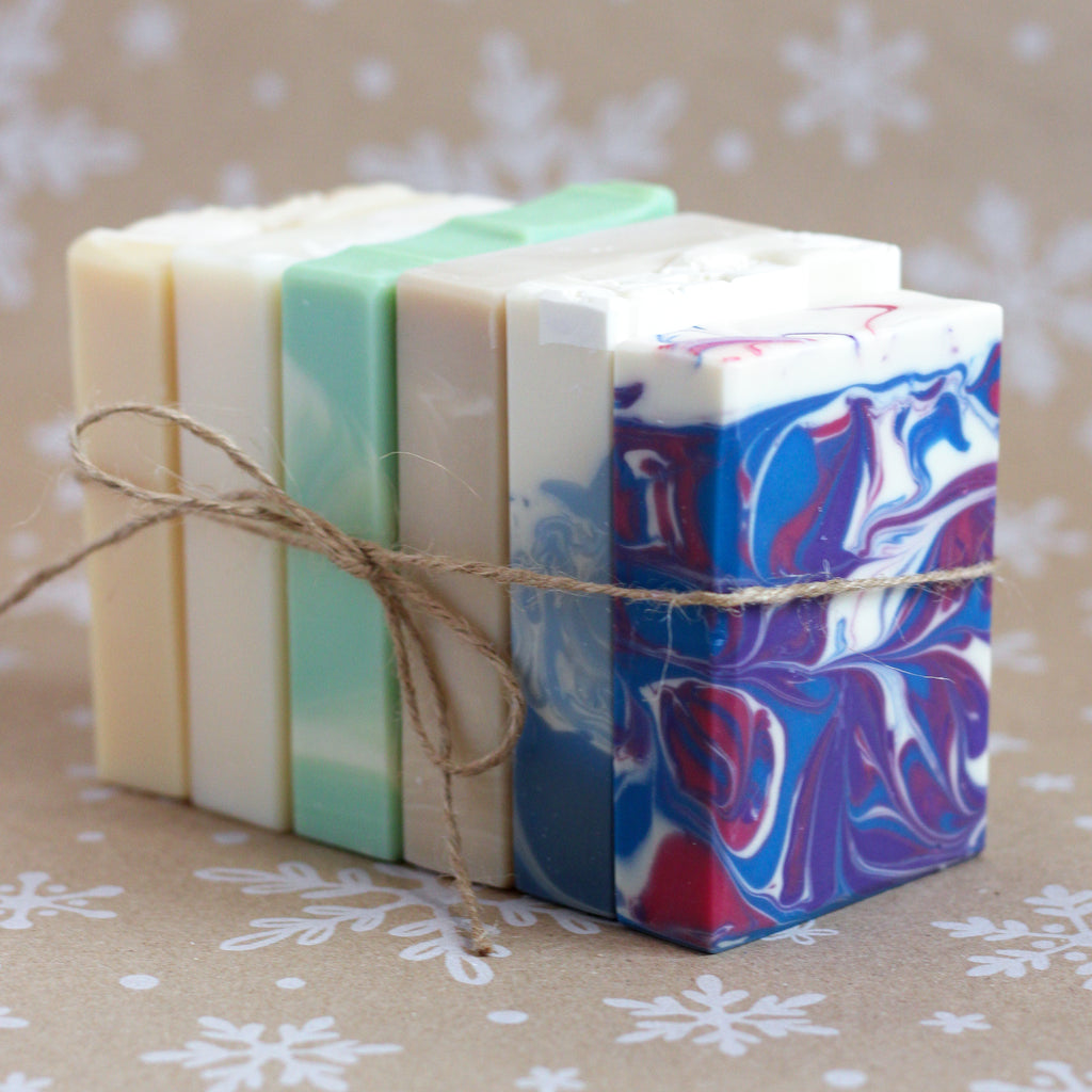 Winter Release Soap Sampler with six wrapped bars tied with twine, on a snowflake-printed kraft background