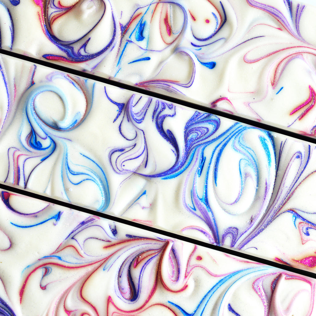 Image of the tops of three Wild Berry Blizzard Soap loaves. Tops are white with swirls of blue, pink, and purple and is topped with glitter.